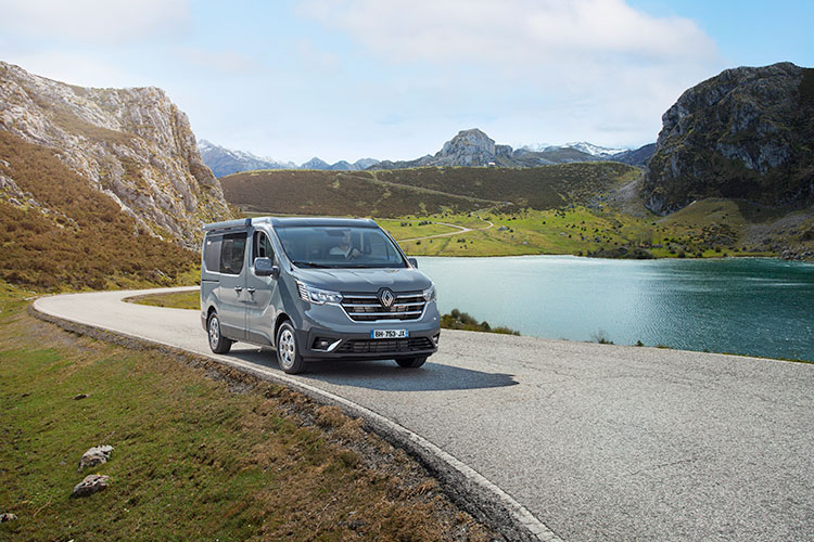 Van aménagé Pilote roulant le long d'un lac dans un paysage montagneux